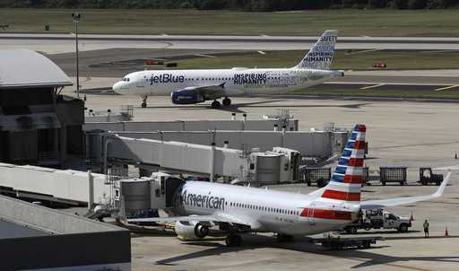 A JetBlue Airbus A320 taxis to a gate on October 26, 2016, after landing, as an American Airlines j…