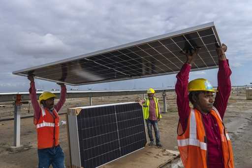 Workers carry a solar panel for installation at the under-construction Adani Green Energy Limited's…