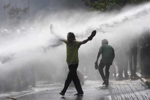 A supporter of Sri Lanka's main opposition holds his shoes in hands as police fire water cannons to…