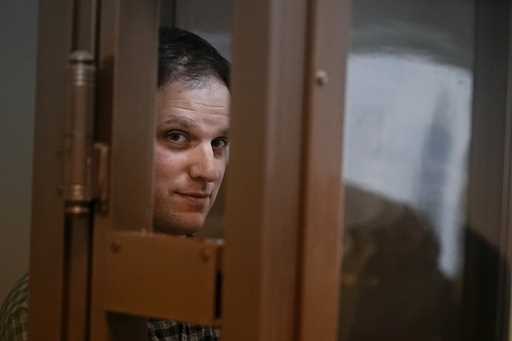 Wall Street Journal reporter Evan Gershkovich stands in a glass cage in a courtroom at the Moscow C…