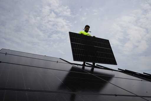 Nicholas Hartnett, owner of Pure Power Solar, holds a panel as his company installs a solar array o…