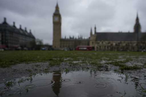 Rain falls into a puddle in Parliament Square, with a backdrop of the Houses of Parliament, in Lond…