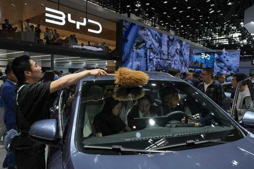 A worker wipes as visitors sit on a BYD Song Pro DM-i car model during the Auto China 2024 in Beiji…