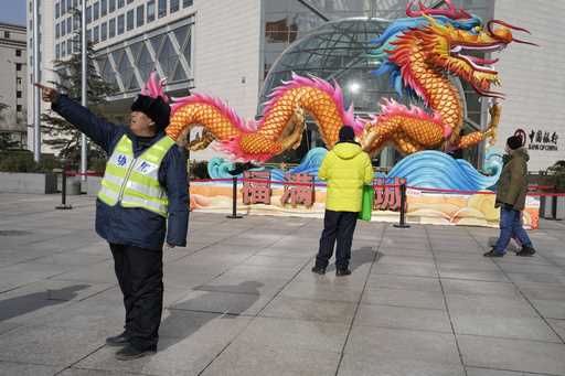A municipal worker gives direction near a sculpture of a dragon in Beijing, Saturday, March 2, 2024…