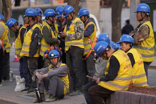 Workers wait for transport outside a construction site in Beijing, Tuesday, April 9, 2024