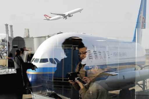Passengers walk past a couple browsing their smartphones near a China Southern Airlines, parked on …