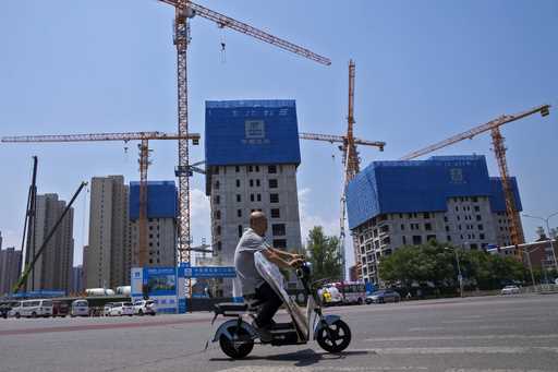 A man rides on an electric bike past by a residential buildings under construction in Beijing on Ju…