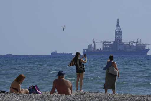 People on the beach take photos of the 'Tungsten Explored' drilling ship, in the southern coastal c…