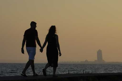 A couple walk by the sea as in the background is seen an apartments tower of a new construction of …