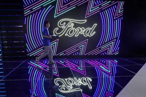 A worker walks past neon signs for Ford at the Auto Shanghai 2023 show in Shanghai, Tuesday, April …