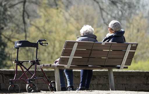 Elderly women sit on a bench beside their walker in the sun at a park in Gelsenkirchen, Germany, We…