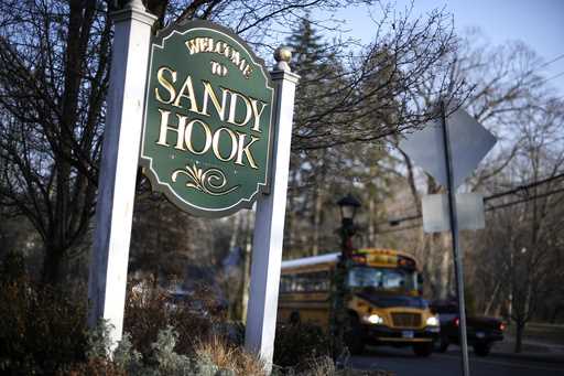 A bus drives past a sign reading Welcome to Sandy Hook in Newtown, Conn