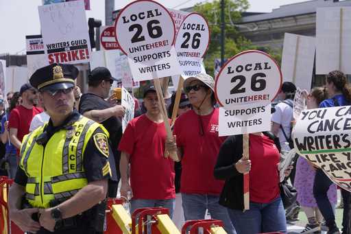 Protesters supporting the Hollywood writers' strike march past a member of law enforcement, left, w…