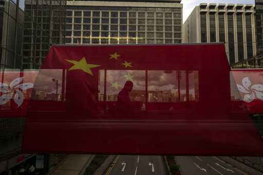 FILE- A pedestrian walks through a footbridge is silhouetted as Chinese and Hong Kong flags are str…
