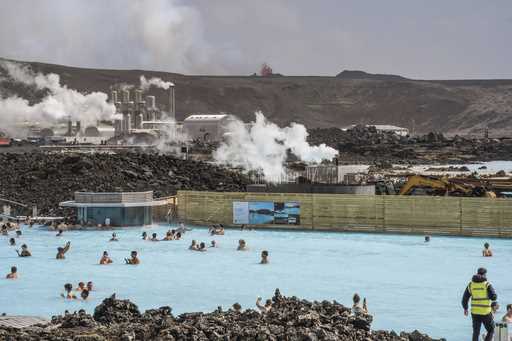 The Blue Lagoon with people bathing in it as the volcanic crater spews lava in the background in Gr…