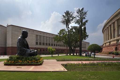 A statue of Mahatma Gandhi sits between the old and new Parliament House buildings on the opening d…