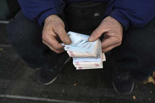 A street money exchanger poses for a photo without showing his face as he counts Iranian banknotes …