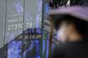 A person stands in front of an electronic stock board showing Japan's Nikkei 225 index at a securit…