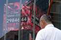 A person walks in front of an electronic stock board showing Japan's Nikkei 225 index at a securiti…