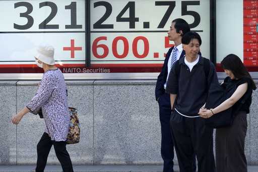 People stand in front of an electronic stock board showing Japan's Nikkei 225 index at a securities…