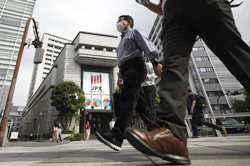 A person walks in front of an electronic stock board showing Japan's Nikkei 225 index at a securiti…