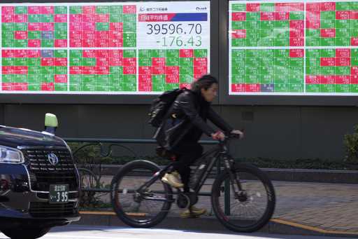 A cyclist moves past an electronic stock board showing Japan's Nikkei 225 index at a securities fir…