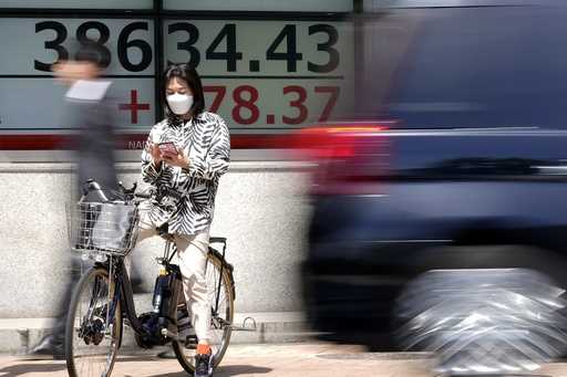A person on a bicycle pauses in front of an electronic stock board showing Japan's Nikkei 225 index…