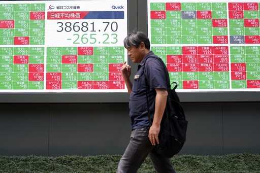 A person walks past an electronic stock board showing Japan's Nikkei 225 index, center, at a securi…