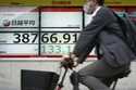 A person rides a bicycle in front of an electronic stock board showing Japan's Nikkei index at a se…