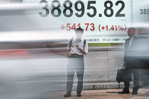 People stand in front of an electronic stock board showing Japan's Nikkei index at a securities fir…