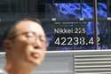 A person walks in front of an electronic stock board showing Japan's Nikkei index at a securities f…