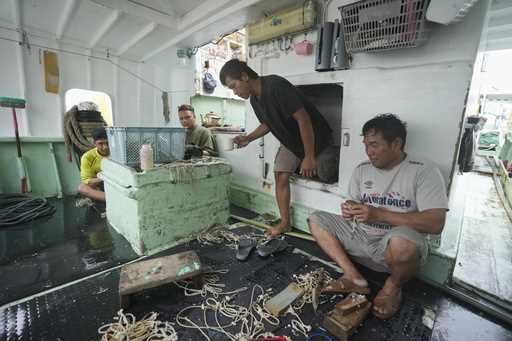 Foreign helpers do some maintenance work on their fishing tools while sitting on their boat docked …