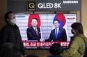People pass by a TV screen showing South Korean President Yoon Suk Yeol, left, meeting with Japanes…