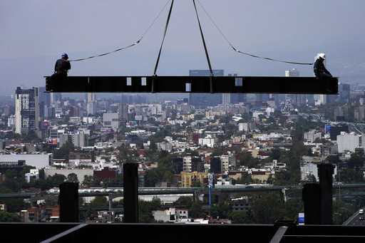 Construction workers ride on a beam hanging from a crane at the construction site of a residential …