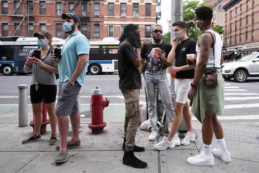 People gather on a street in the Hell's Kitchen neighborhood of New York while waiting to get takeo…