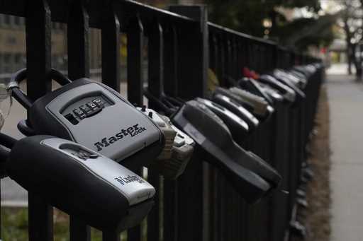 Key lock boxes for real estate showings hang on a fence outside a high-rise condominium building, O…
