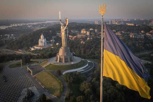 The national flag waves as workers install the Ukrainian coat of arms on the shield in the hand of …