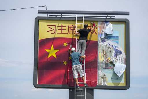 Workers hang on ropes to install a giant Chinese national flag on a skyscraper that is a symbolic g…