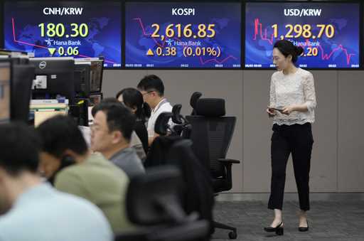 A currency trader passes by screens showing the Korea Composite Stock Price Index…