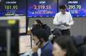 A currency trader passes by the screens showing the Korea Composite Stock Price Index…