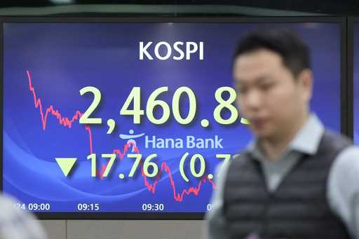 A currency trader walks by the screens showing the Korea Composite Stock Price Index…