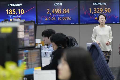 A currency trader passes by the screens showing the Korea Composite Stock Price Index…