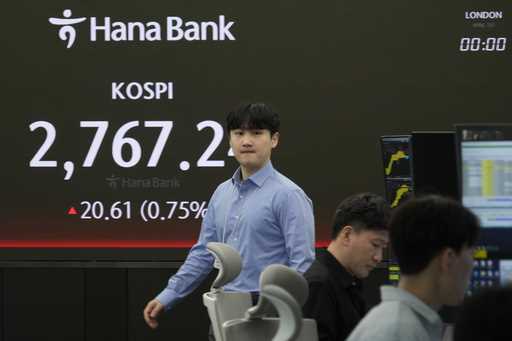 A currency trader walks by the screen showing the Korea Composite Stock Price Index…