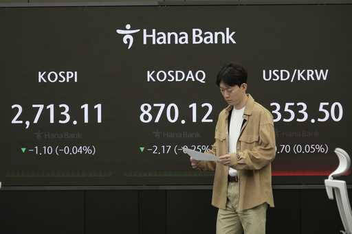 A currency trader passes by the screen showing the Korea Composite Stock Price Index…