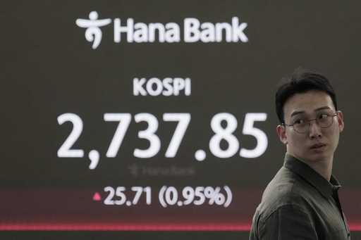 A currency trader works near the screen showing the Korea Composite Stock Price Index…