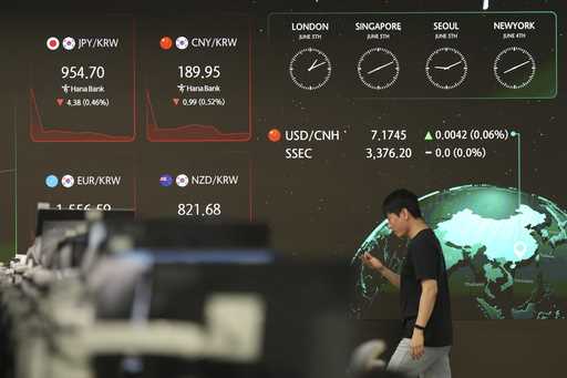 A dealer walks past near the screens showing the foreign exchange rates at a dealing room of Hana B…