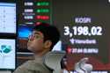 A currency trader watches monitors near a screen showing the Korea Composite Stock Price Index…