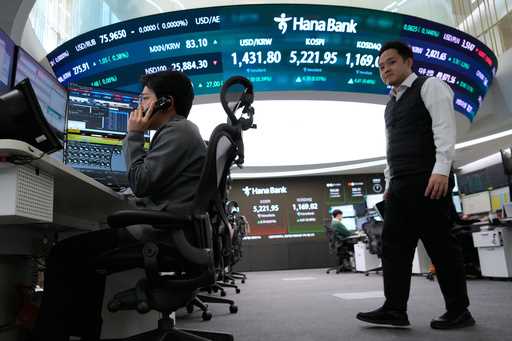 A currency trader talks on the phone near a screen showing the Korea Composite Stock Price Index…