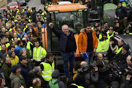 A woman crosses a street as farmers with their tractors attend a protest in Pamplona, northern Spai…