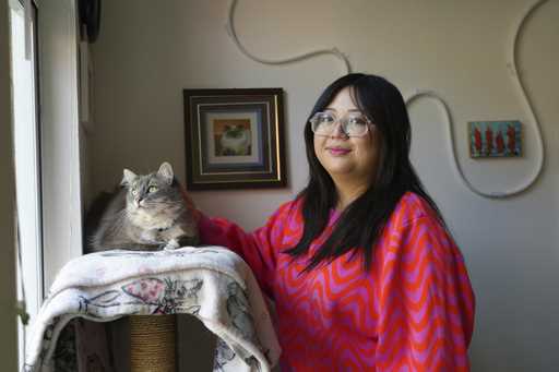 Celina Chanthanouvong stands with her cat in her apartment in Emeryville, Calif